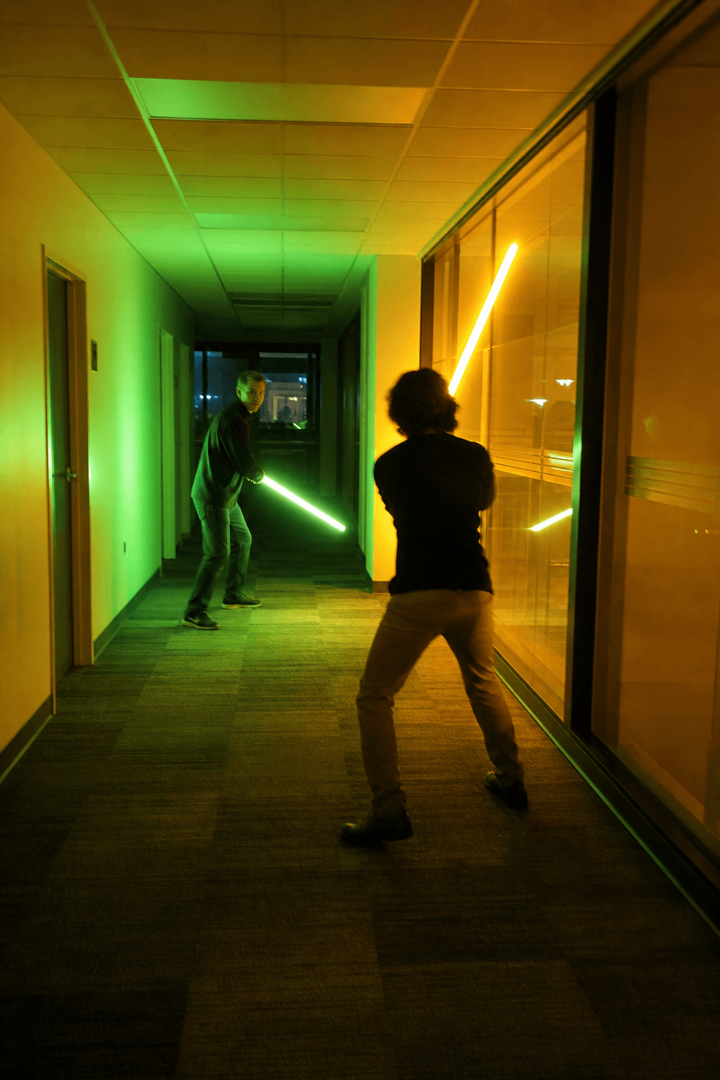 Two people in an office corridor holding glowing energy blades