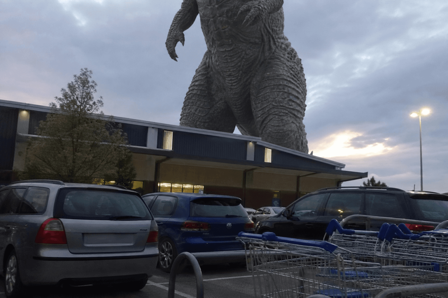 A supermarket car park with a colossal monster standing behind the store